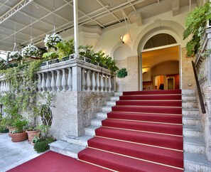 Un magnifique escalier, avec des marches recouvertes de moquette rouge, menant à une porte en arc de cercle.