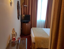Hotellihuone, jossa on sänky, työpöytä, kahvinkeitin ja kuppi, kaapissa oleva televisio ja verhot.