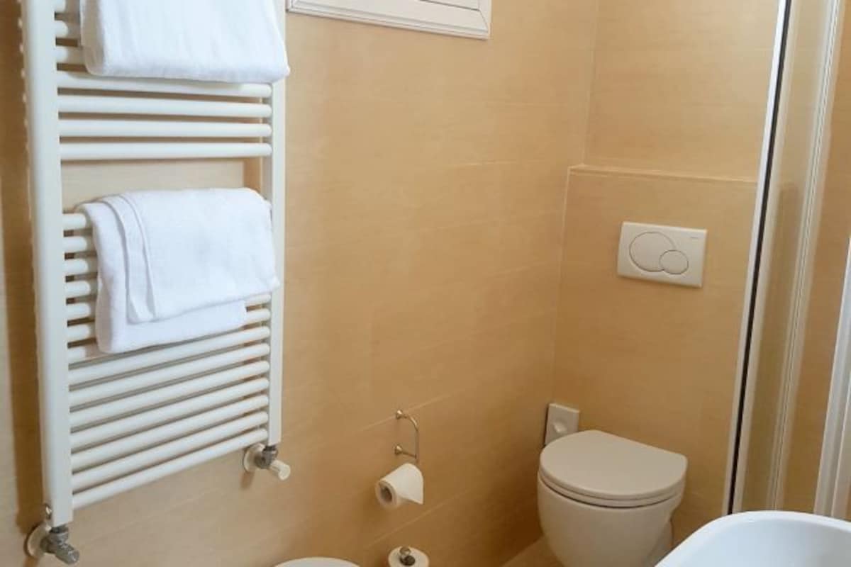 Un baño con inodoro, toallero con toallas, ducha e interruptor de luz en la pared.