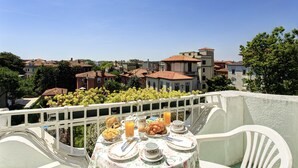 Un balcón con una mesa dispuesta para el desayuno, con vistas a una zona residencial con casas y vegetación.