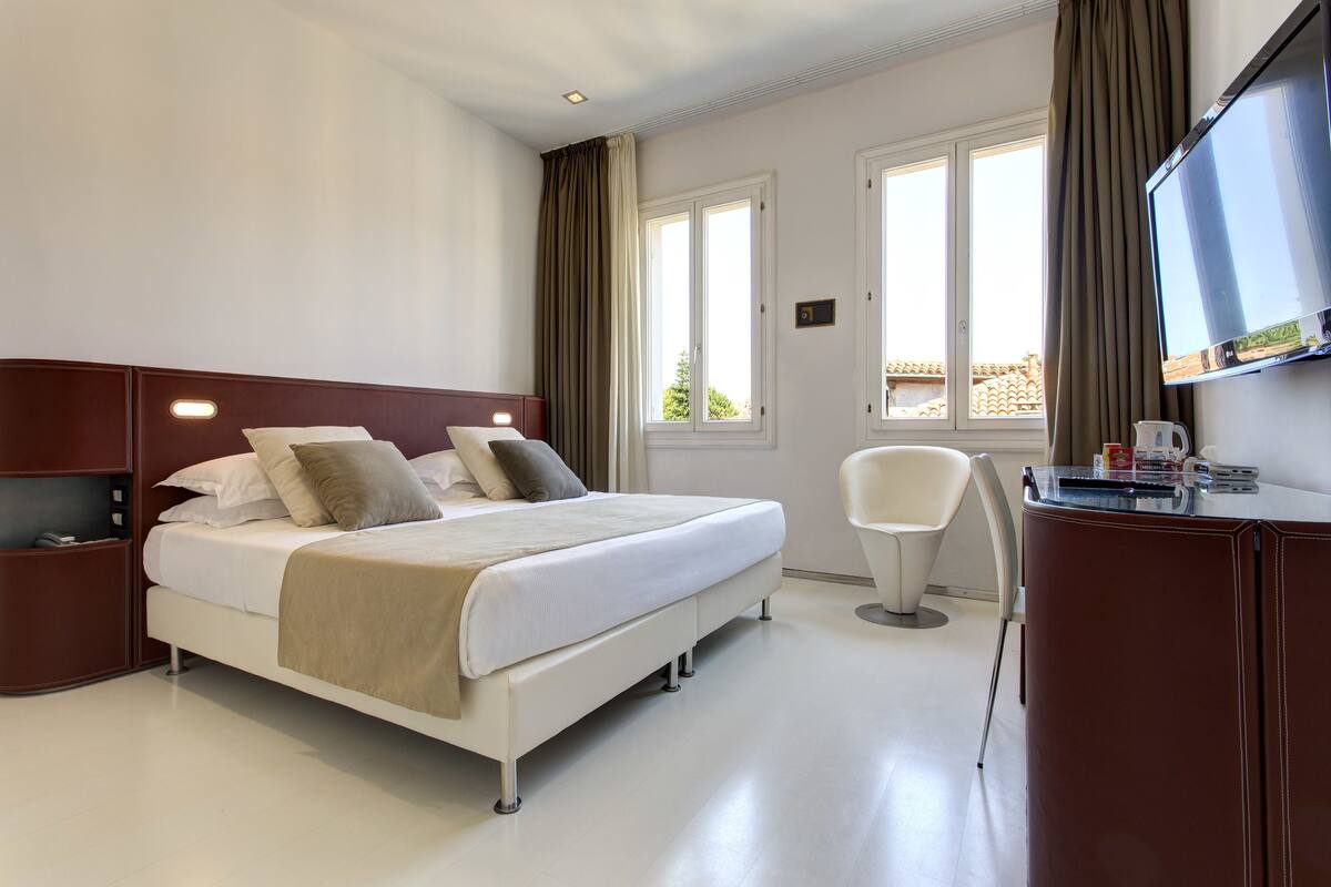 A modern hotel room with a bed, a desk, a chair, and a TV.