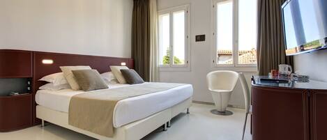 A hotel room with a bed, a desk, a chair, a TV, and a window with curtains.