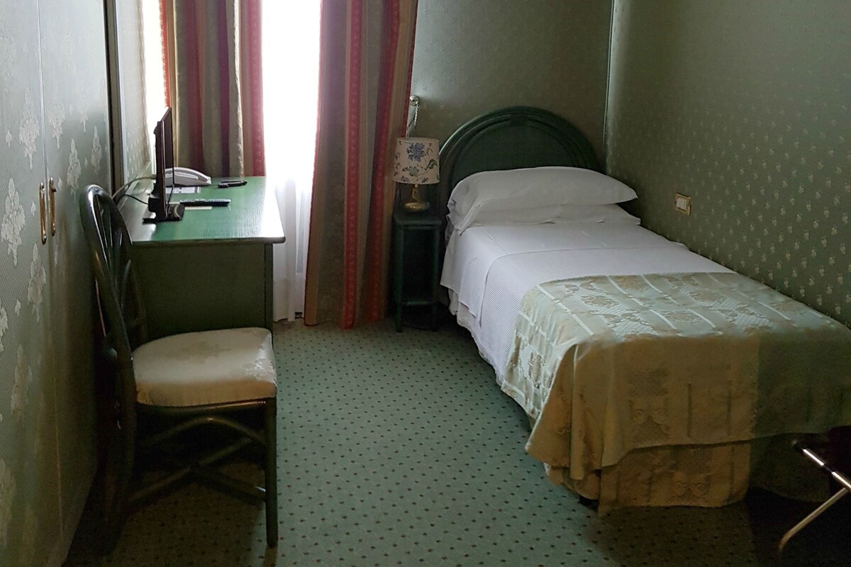 A small, compact room with a single bed, a desk, and a chair.