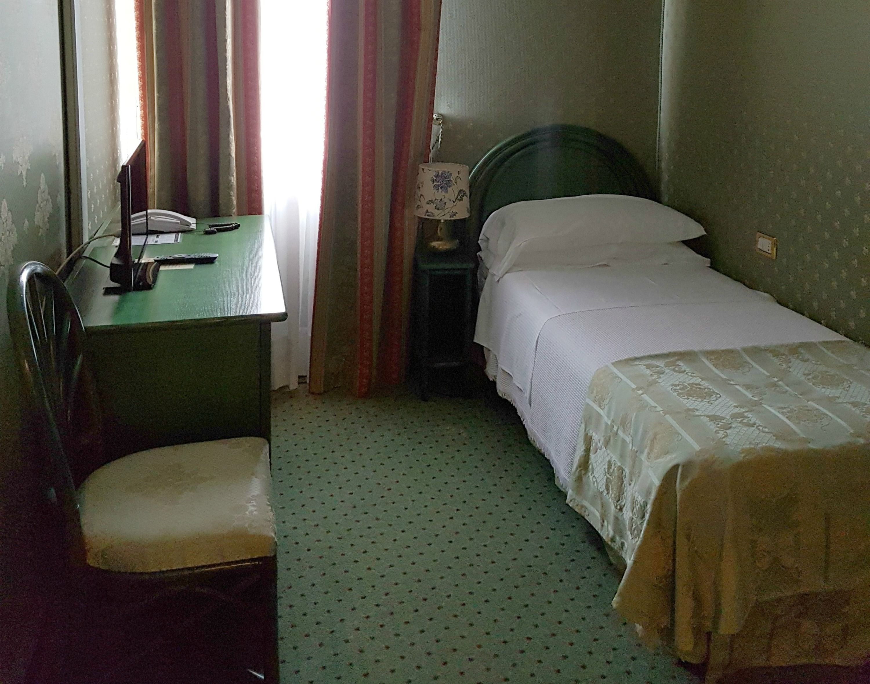 Une petite pièce simple, avec un bureau, une chaise et un lit simple.