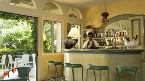 Zona de bar con un bartender, taburetes verdes y una barra con diferentes botellas.