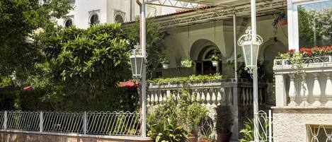 A covered outdoor area with a red carpet, potted plants, and a white railing.