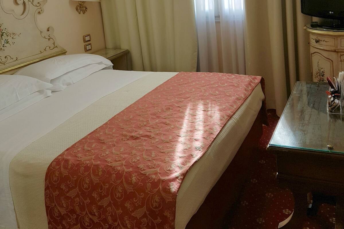 A hotel room with a bed, a desk, a television, and curtains.