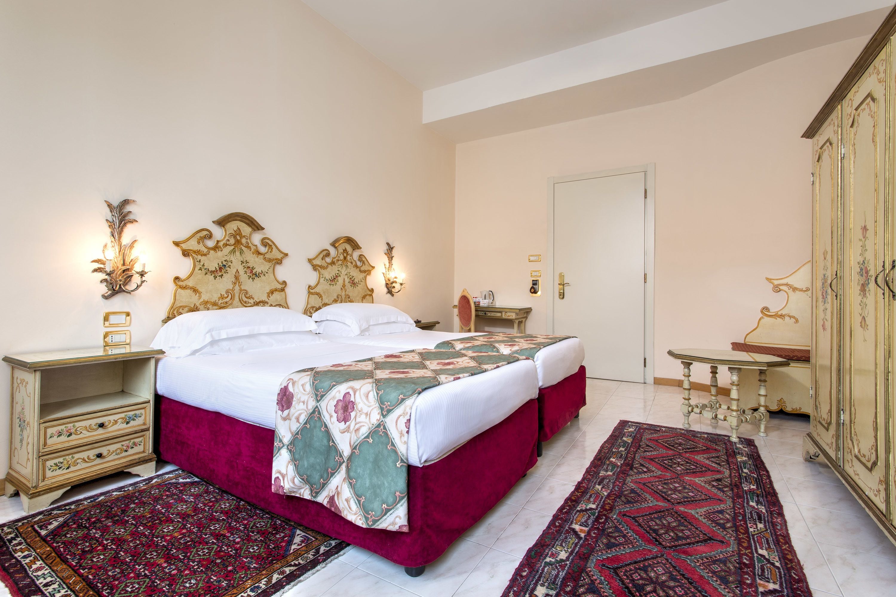 A spacious bedroom with a large bed, two bedside tables, a wardrobe, and two rugs.