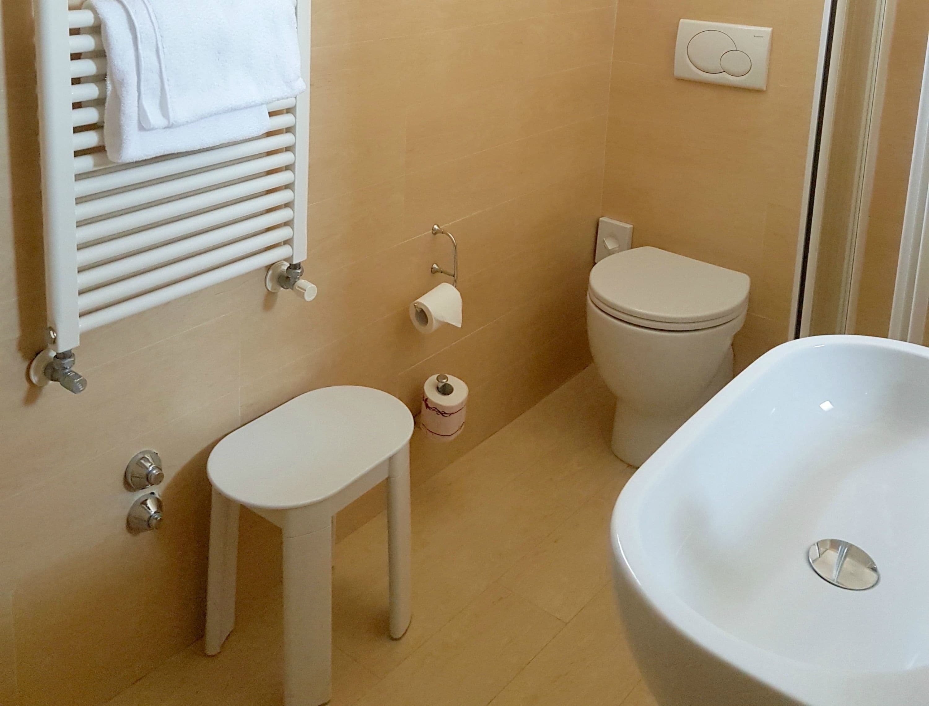 Un bagno con un water bianco, un lavandino bianco e una vasca da bagno bianca. C'è un portascopevoli con un asciugamano appeso, e un porta carta igienica con un rotolo di carta igienica.