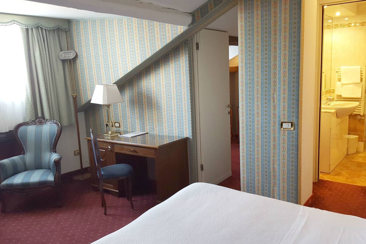 A hotel room with a bed, a desk, a chair, and a bathroom visible through an open door.
