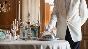 Un elegante ambiente de comedor con un camarero con traje blanco, una mesa con mantel blanco, velas y cubertería.