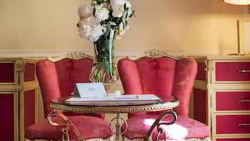 A room with a round table, two chairs, a vase of flowers, and a lamp.
