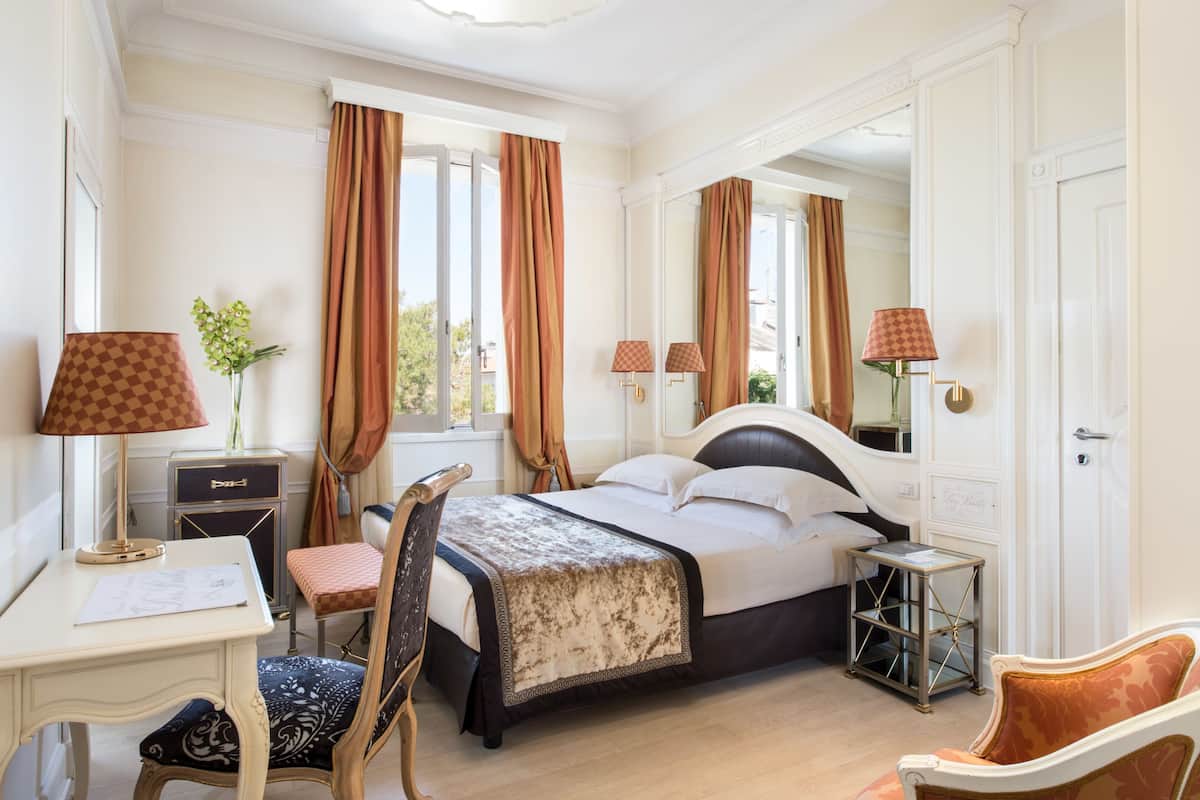 Habitación de hotel con cama, escritorio, silla, lámpara y una mesita.