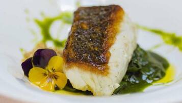 Un plato blanco con un trozo de pescado, salsa verde y una flor.