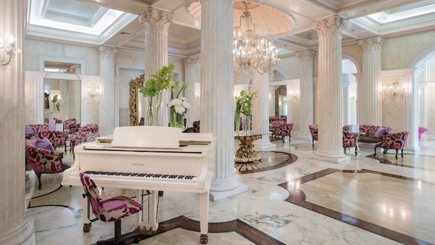 Un amplio hall de entrada con un piano de cola, columnas ornamentales y asientos mullidos.