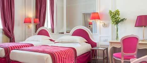 A hotel room with two beds, a desk, a chair, a mirror, and a vase with flowers.