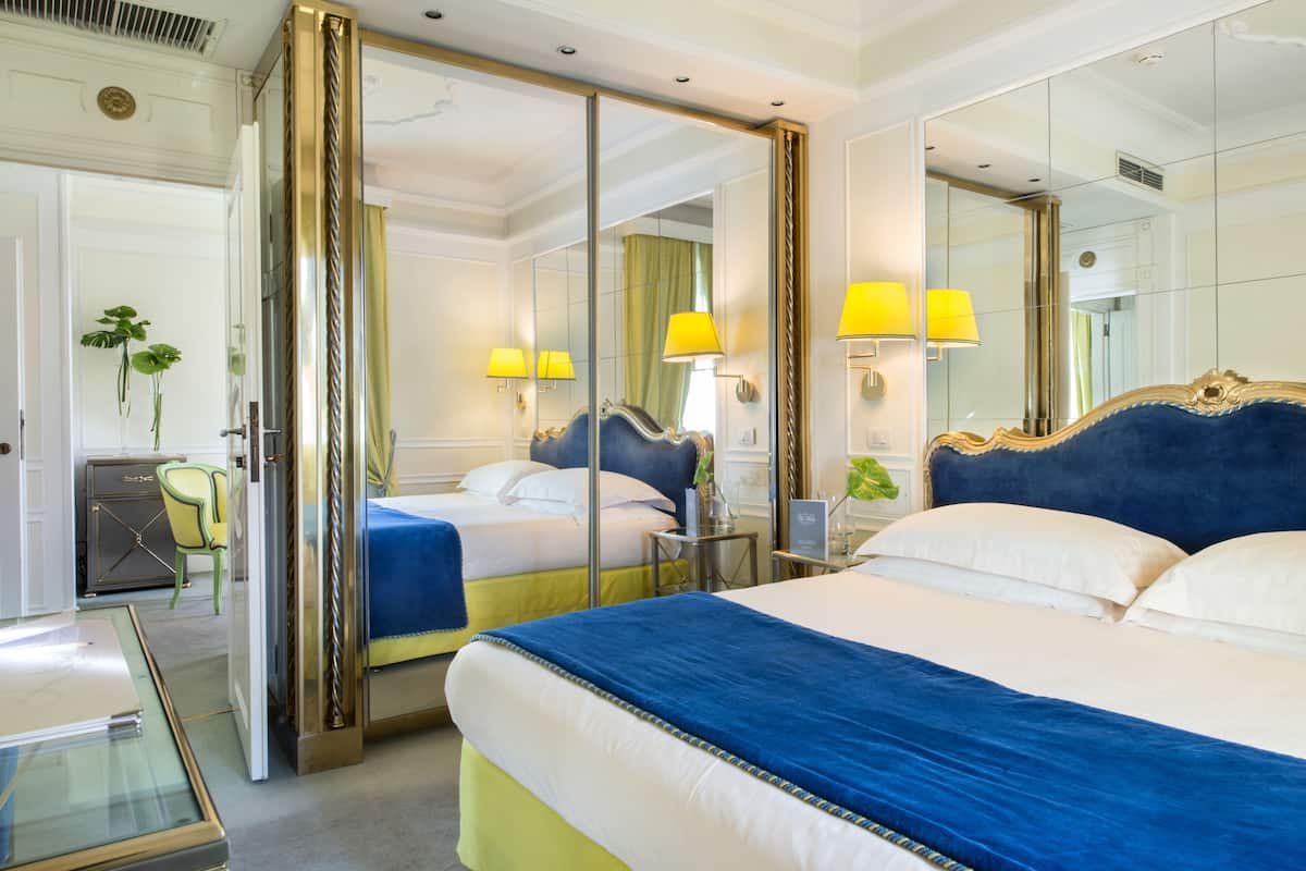 Habitación de hotel con dos camas, un espejo grande y un escritorio con lámpara.
