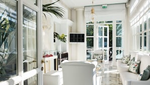 Habitación amplia y bien iluminada con un ventanal grande, televisión y zona de estar con mobiliario blanco.