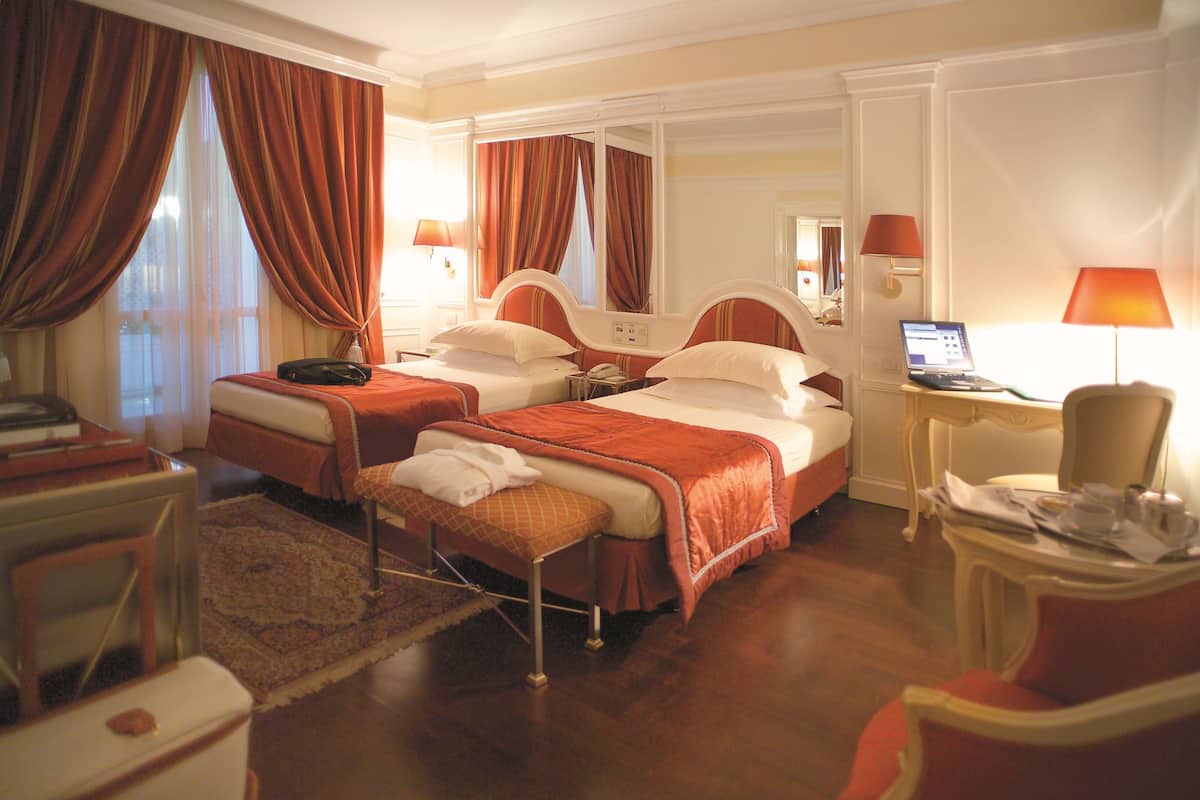 Habitación de hotel con dos camas, un escritorio, una silla, una computadora portátil y una ventana con cortinas.