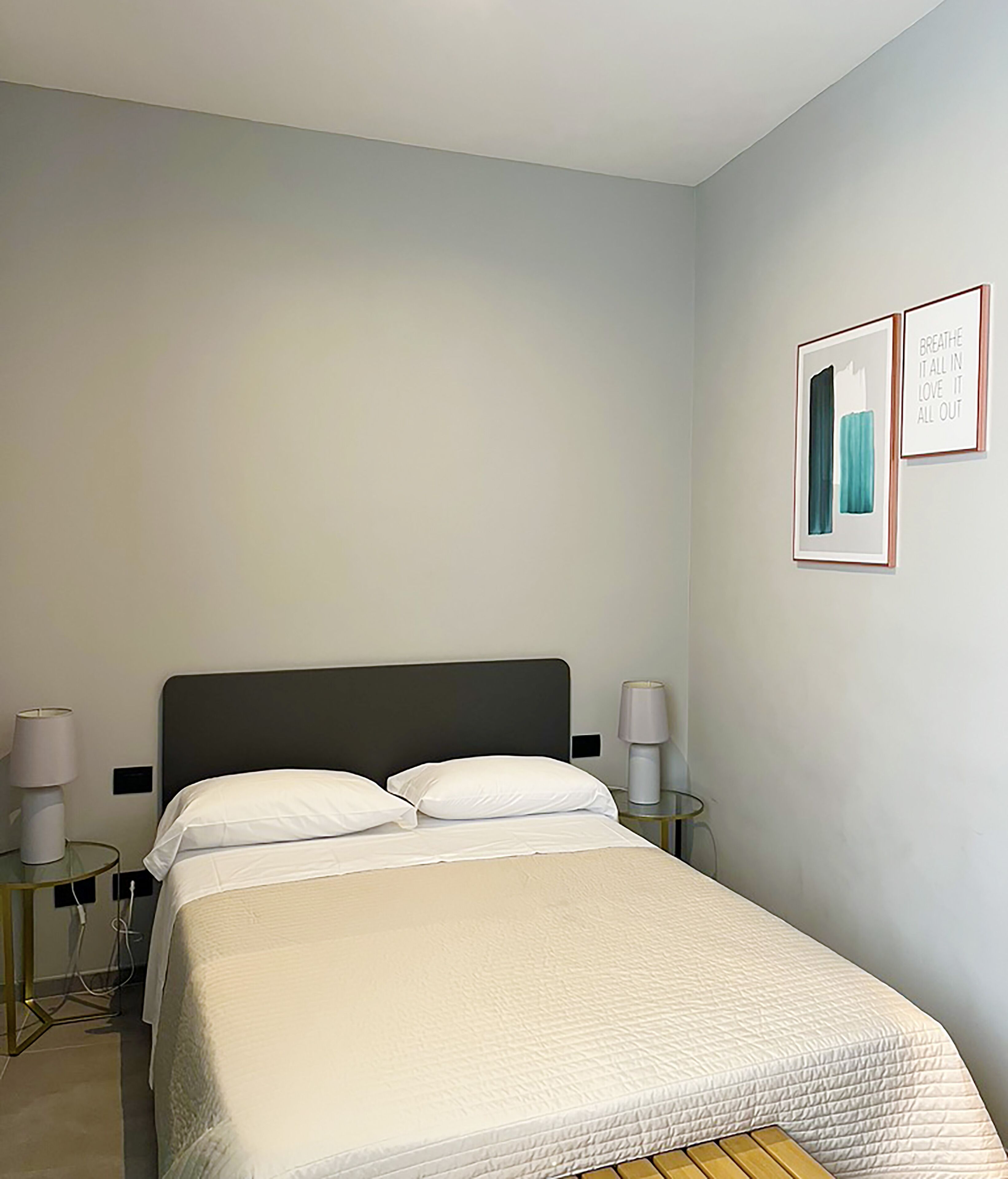 A neatly made bed with white linens, a dark headboard, and two bedside tables with lamps.