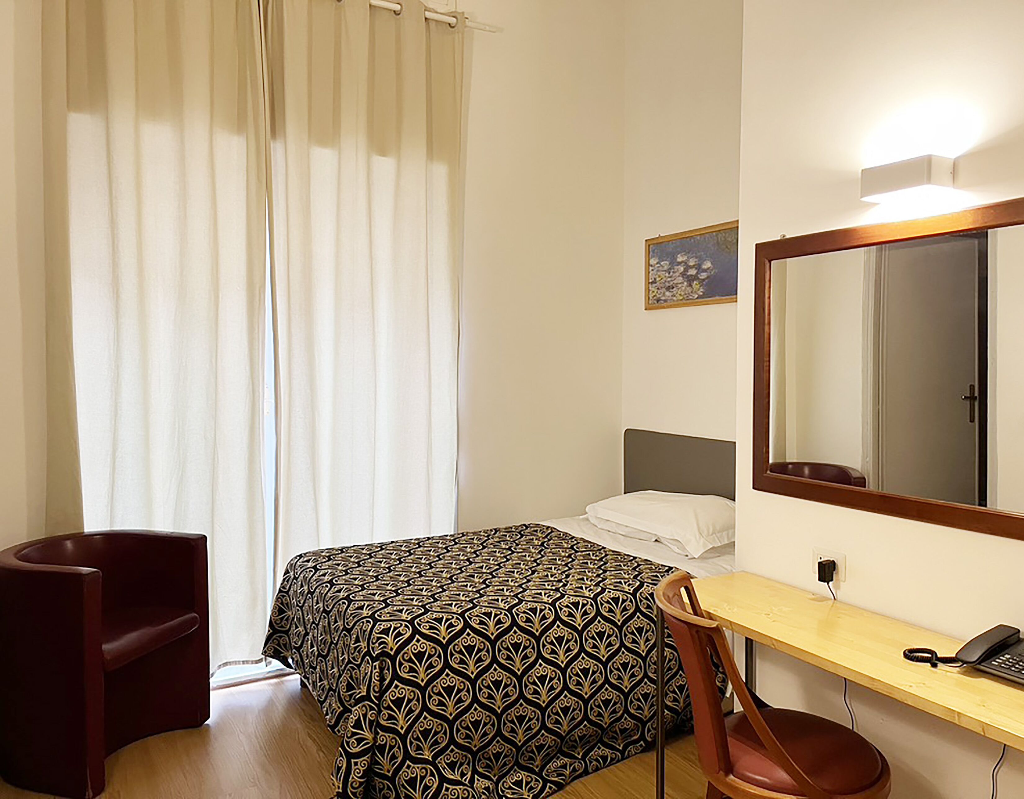 Habitación de hotel con cama, escritorio, silla, espejo y ventana con cortinas.