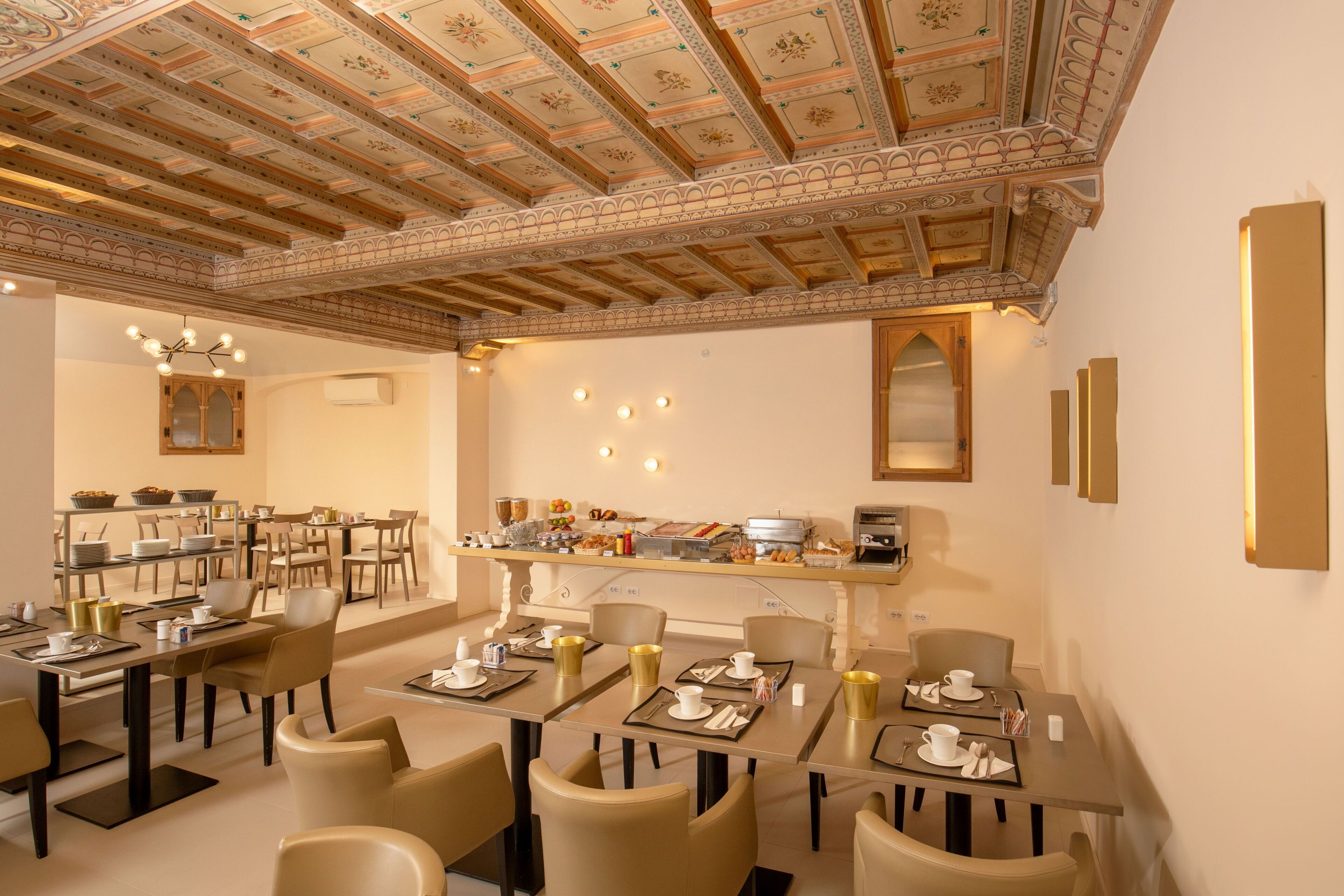 A dining area with multiple tables and chairs, a buffet setup, and a decorative ceiling.