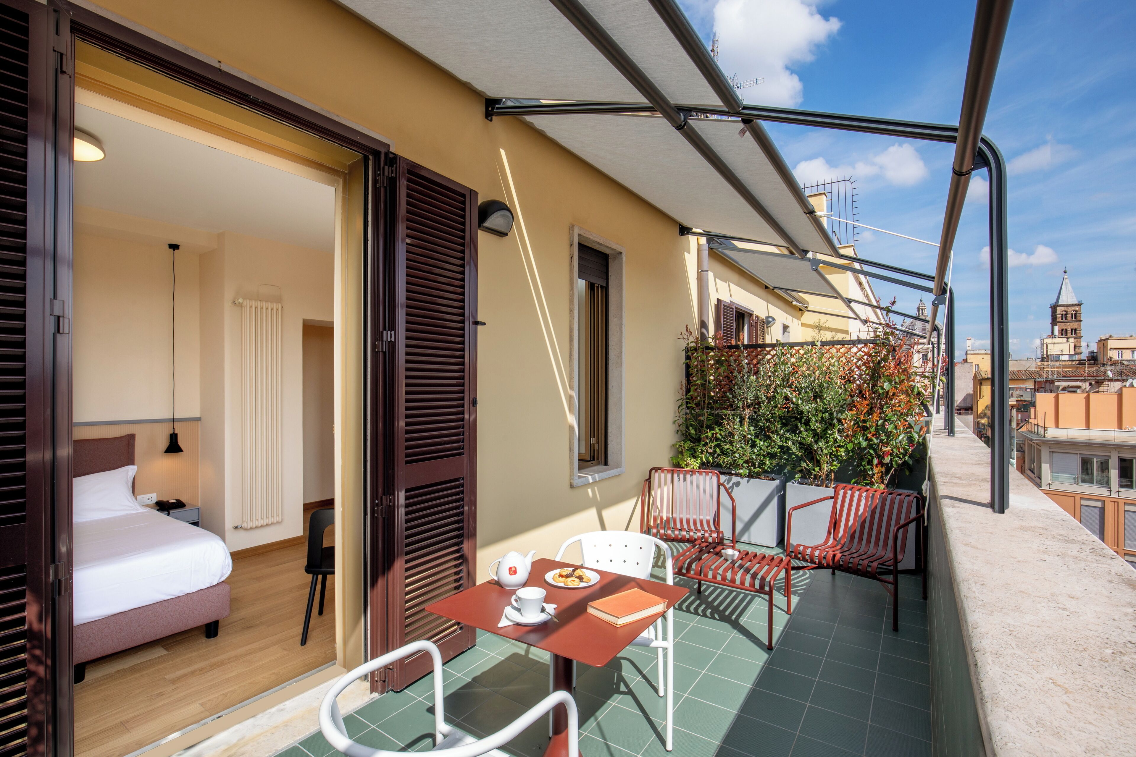 Un balcon avec un lit, une table avec une théière et un livre, et une chaise.