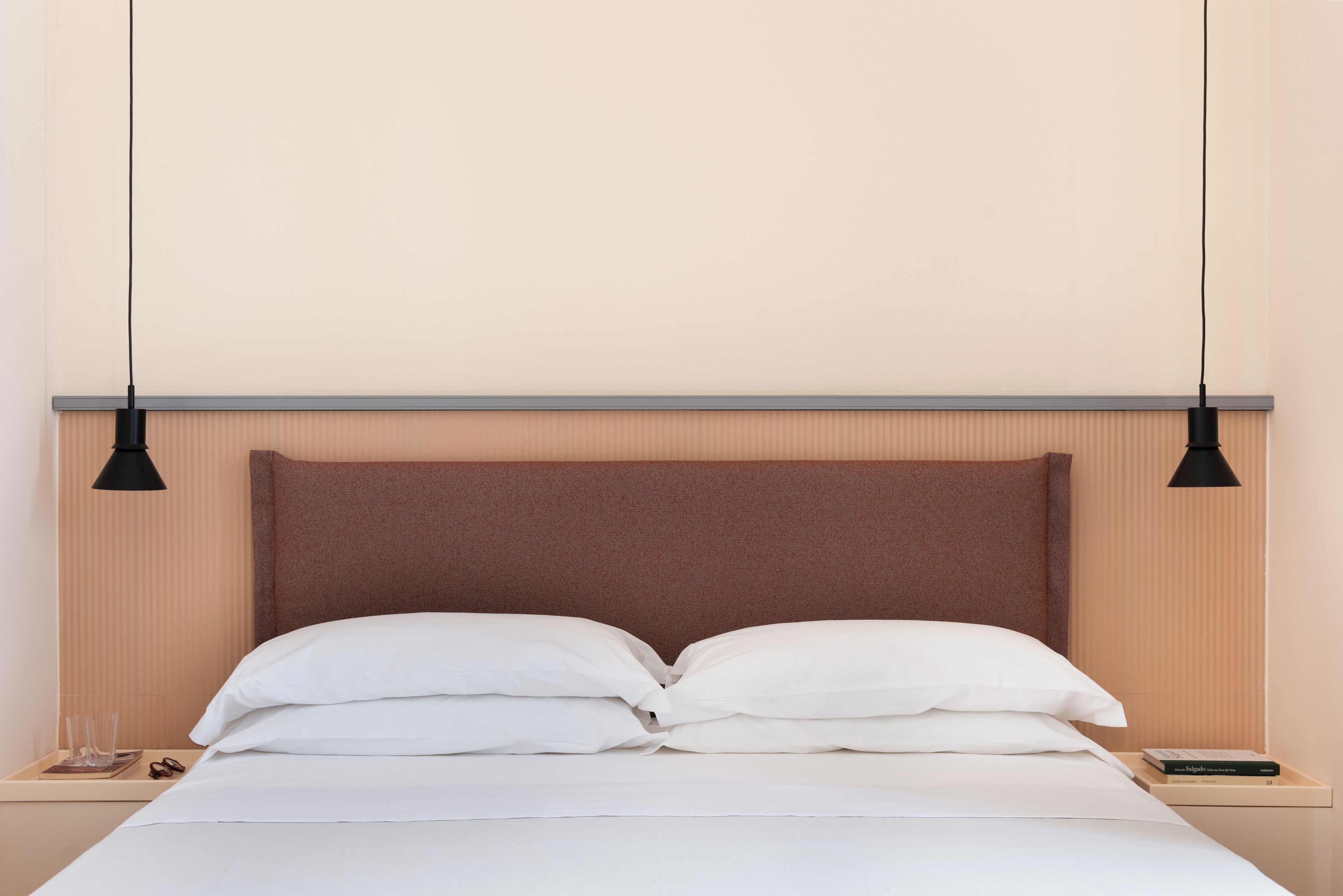 Ein ordentlich bezogenes Bett mit weißen Leinen, einem braunen Kopfteil und zwei Nachttischlampen.