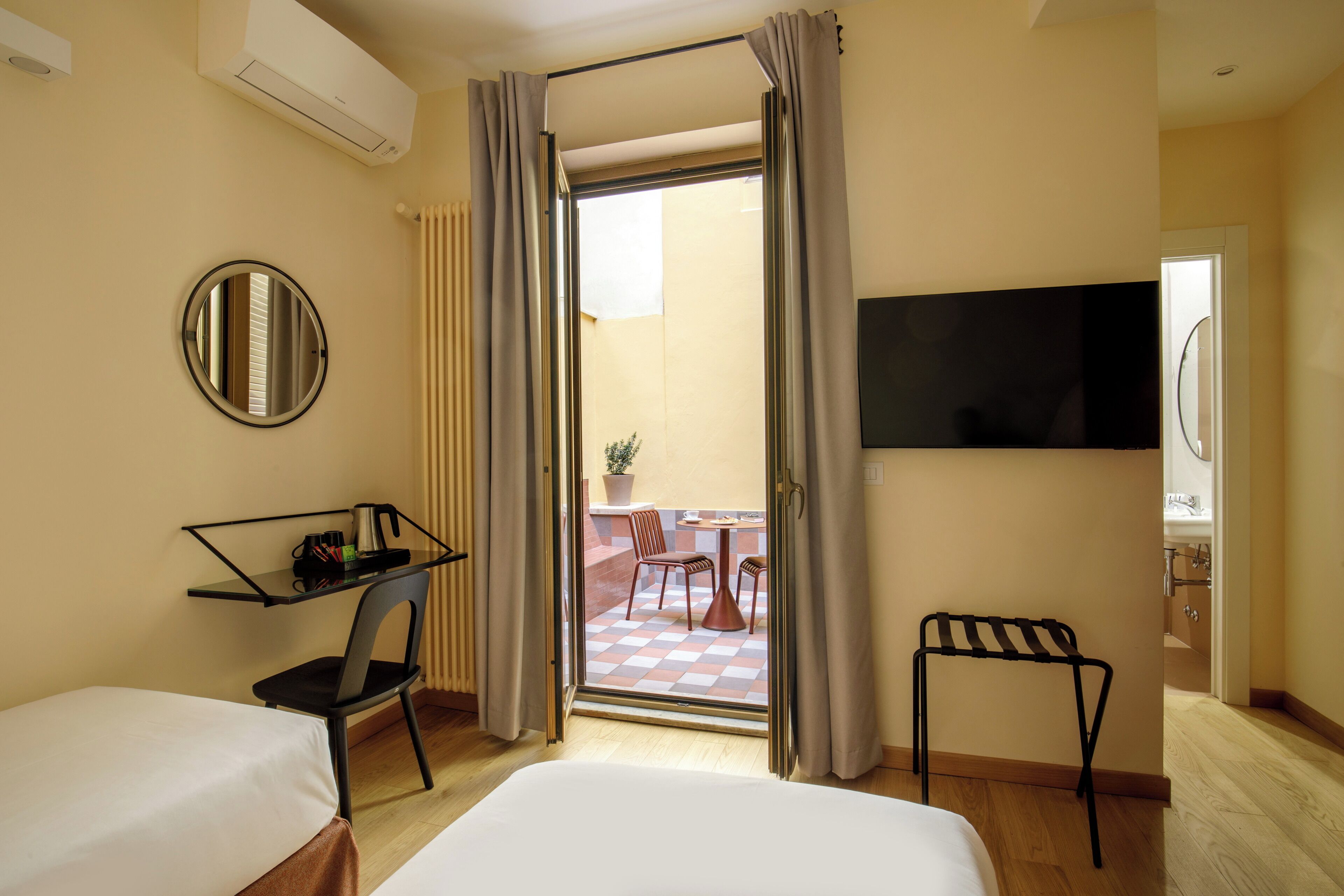 Een hotelkamer met een bed, een bureau met stoel, een aan de muur bevestigde televisie en een balkon met een geruite vloer en stoelen.