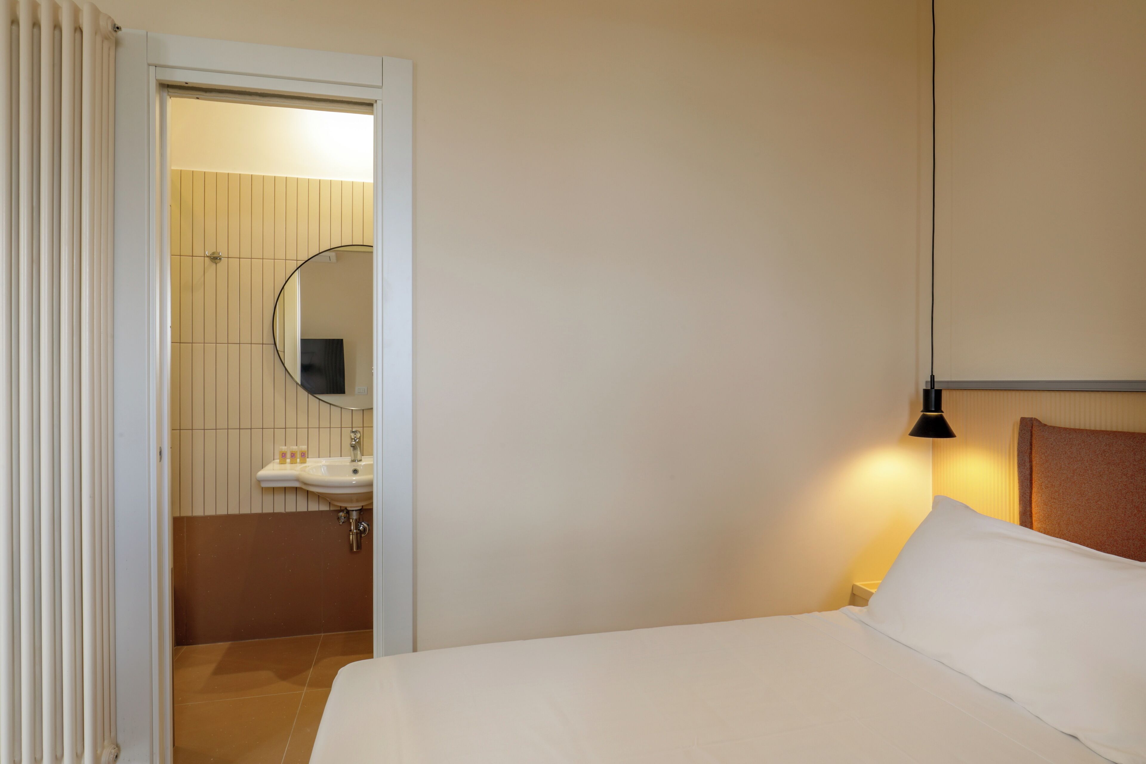 Hotelkamer met een bed, een bedlamp, een badkamer met wastafel en spiegel, en een deur naar een andere kamer.