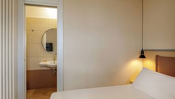 Hotelkamer met een bed, een bedlamp, een badkamer met wastafel en spiegel, en een deur naar een andere kamer.