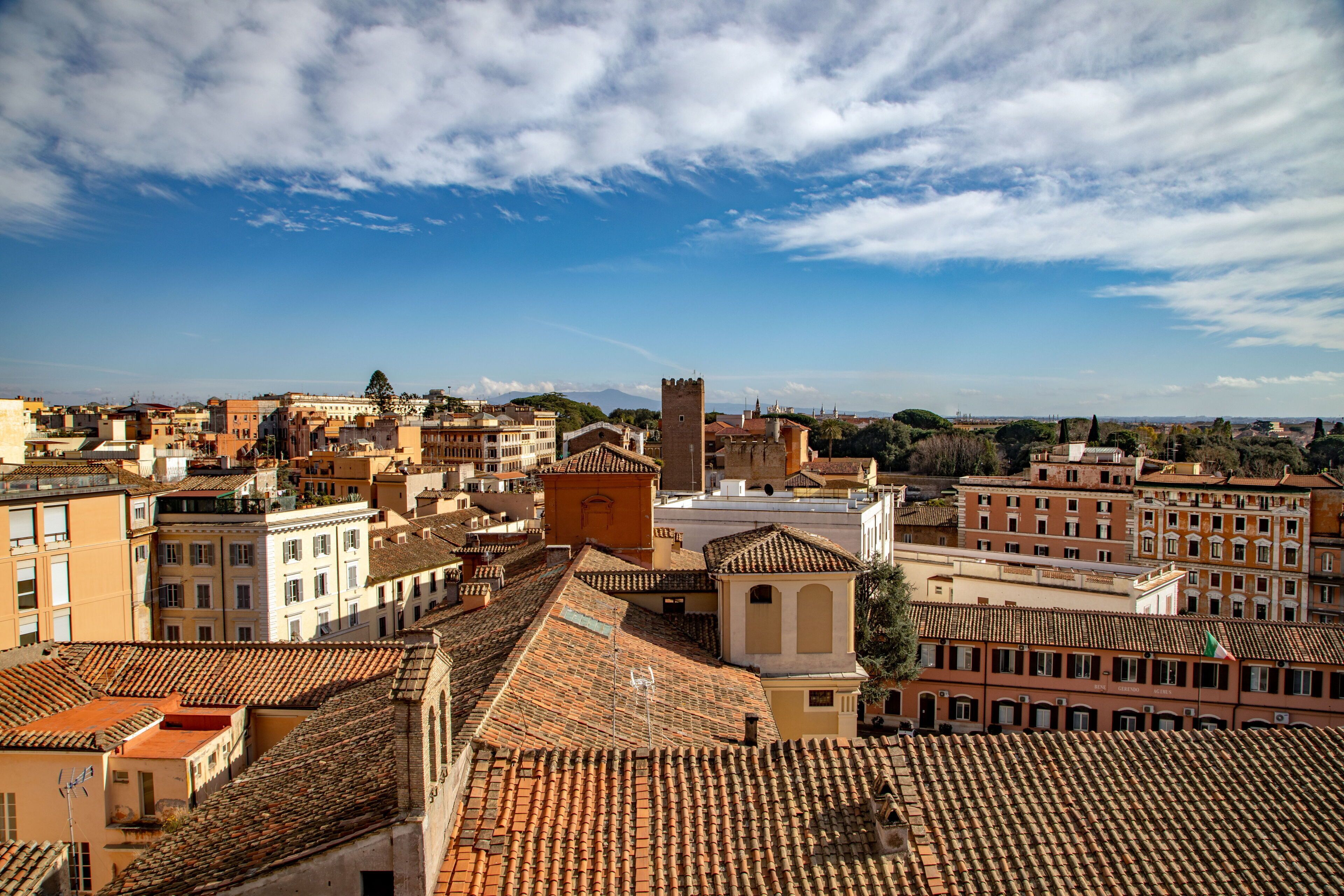 A cityscape with terracotta-tiled rooftops, historic buildings, and a prominent tower.