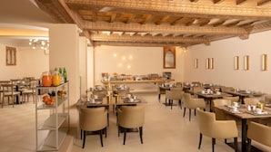 Un comedor amplio con varias mesas y sillas, una barra de buffet con comida y bebidas, y un techo decorativo con diseños intrincados.