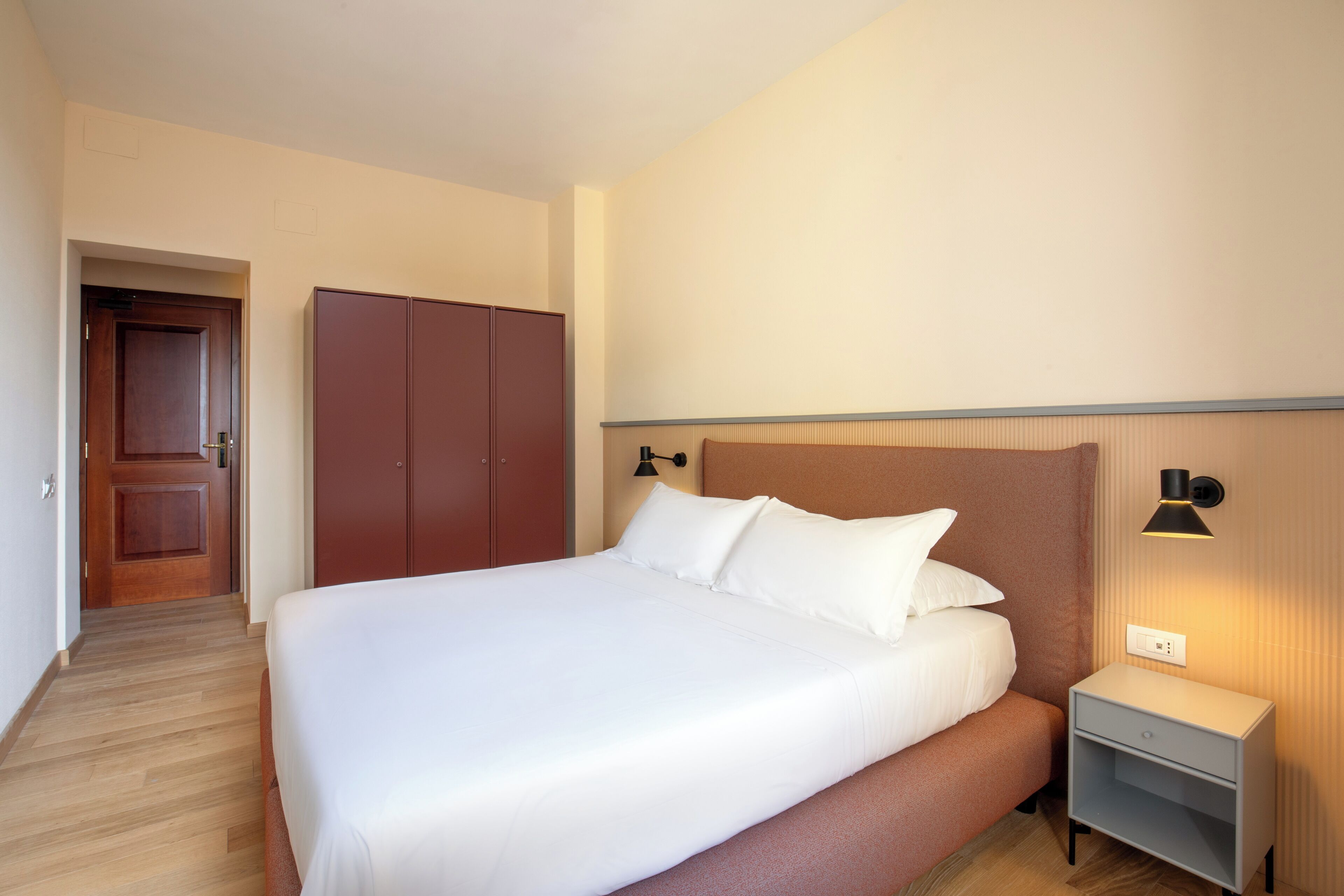 Una habitación de hotel con una cama grande, una mesita de noche, un armario y una puerta que da a otra habitación.