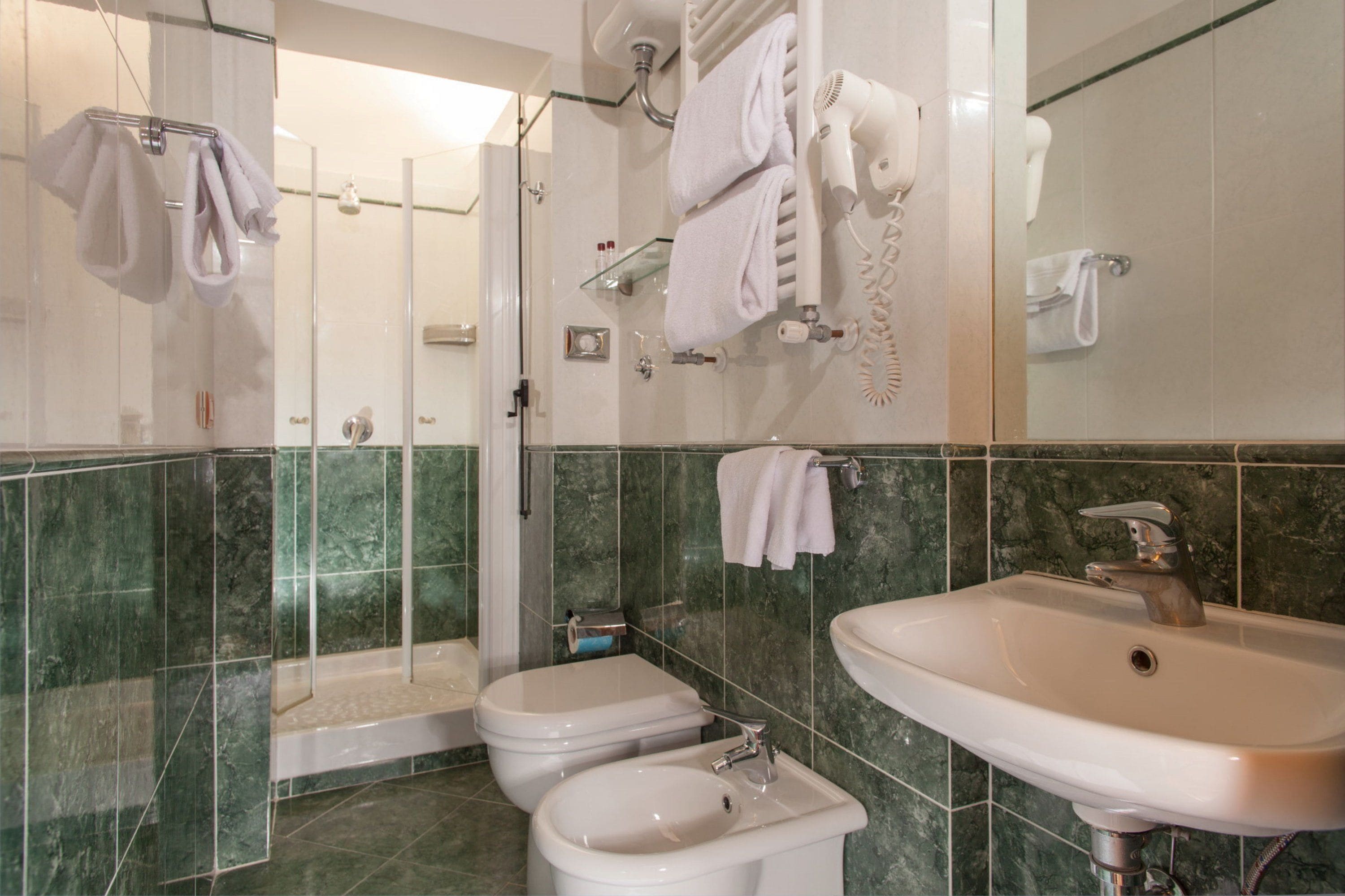 A modern bathroom with a glass shower enclosure, a white sink, and two toilets.