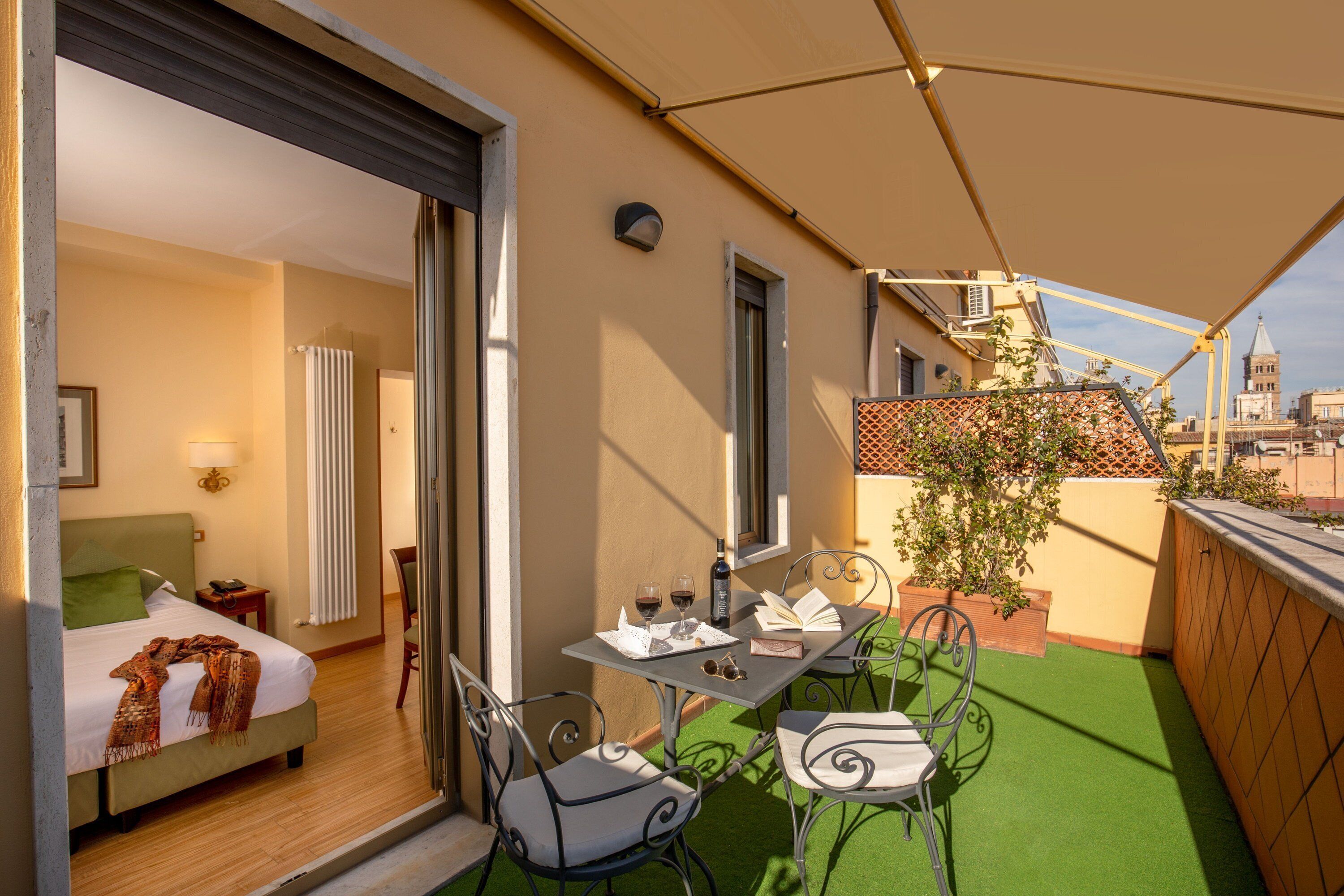 A balcony with a table, chairs, and a bed inside a room.