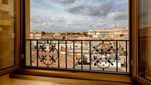 Vista desde una ventana con barandillas de metal ornamentadas, sobre un paisaje urbano con edificios históricos y un cielo despejado.