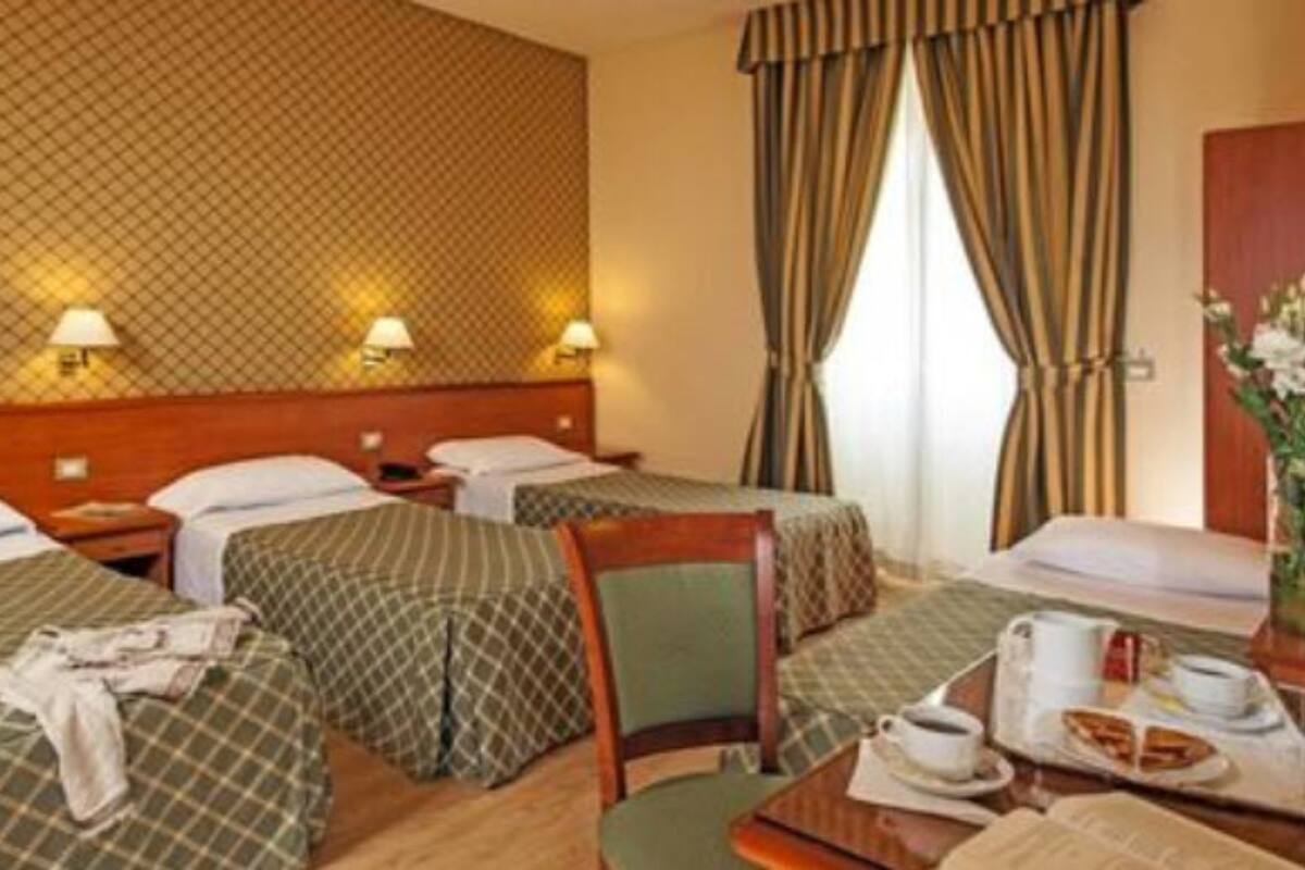 Hotellihuone, jossa on kaksi sänkyä, pieni pöytä, jossa on kuppi ja lautanen, sekä tuoli.