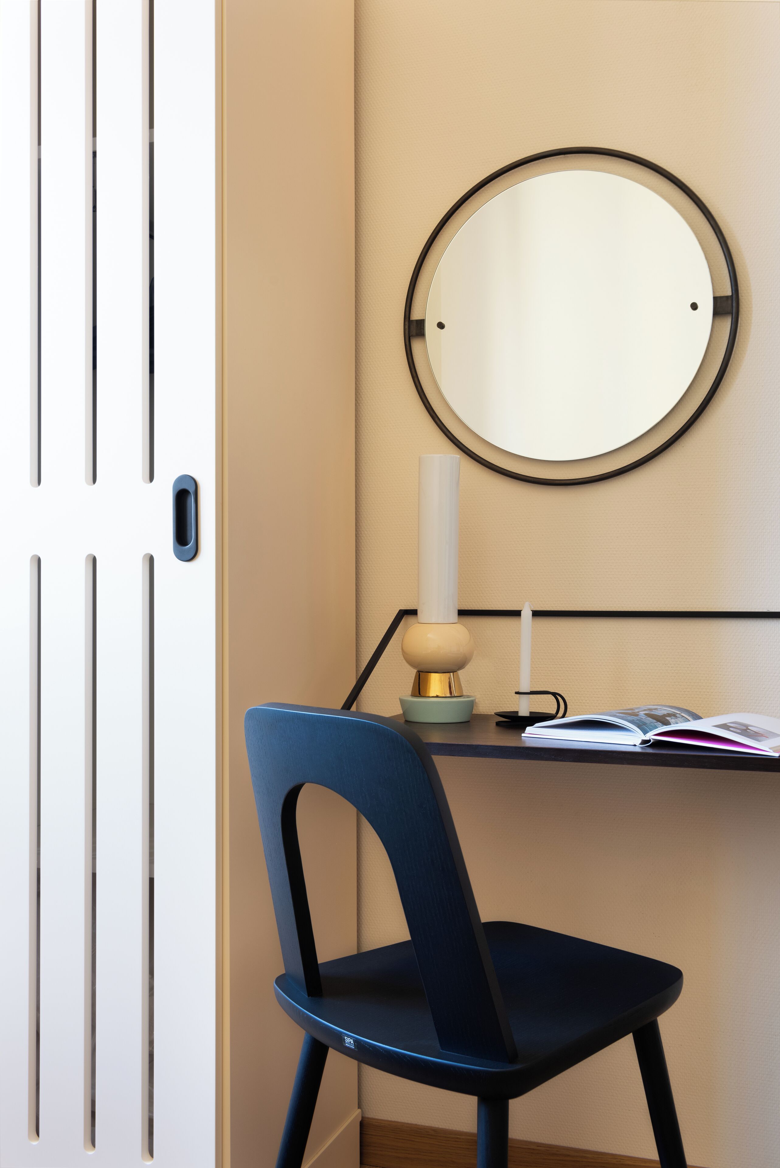Une pièce comprenant un bureau, une chaise, un miroir rond, une bougie et un livre.