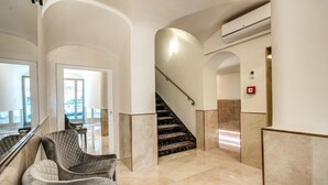 Un amplio vestíbulo con suelo de mármol, una escalera y una zona de estar con sillones acolchados.