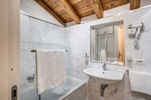 A modern bathroom with a glass-enclosed shower, a marble sink, and a hairdryer mounted on the wall. - Hotel San Silvestro (Rome)