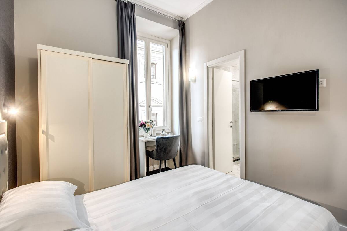 A hotel room with a bed, a desk, and a TV.
