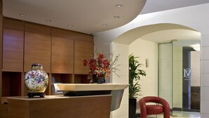 A modern reception area with a wooden reception desk, a vase with flowers, and a potted plant. - Hotel Memphis (Rome)