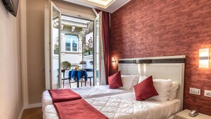 A hotel room with two beds, red and white bedding, a nightstand with a phone, and a view of the street outside. - Hotel Memphis (Rome)