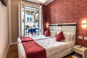 A hotel room with two beds, red and white bedding, a nightstand with a phone, and a view of the street outside.