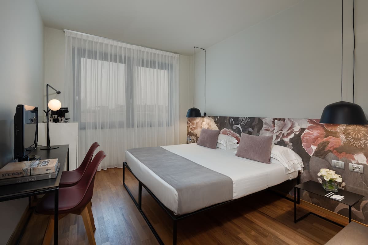 A modern hotel room with a bed, a desk, a chair, and a nightstand.