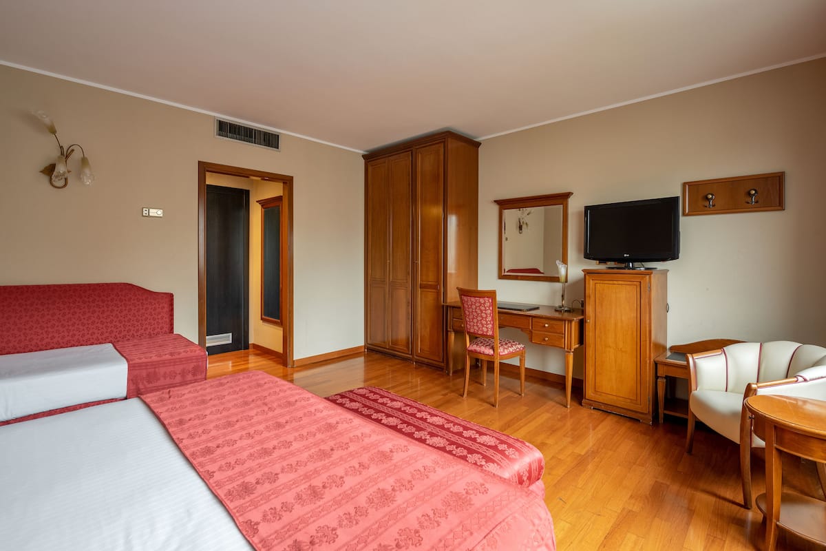 A hotel room with two beds, a desk, a chair, a television, and a wardrobe.
