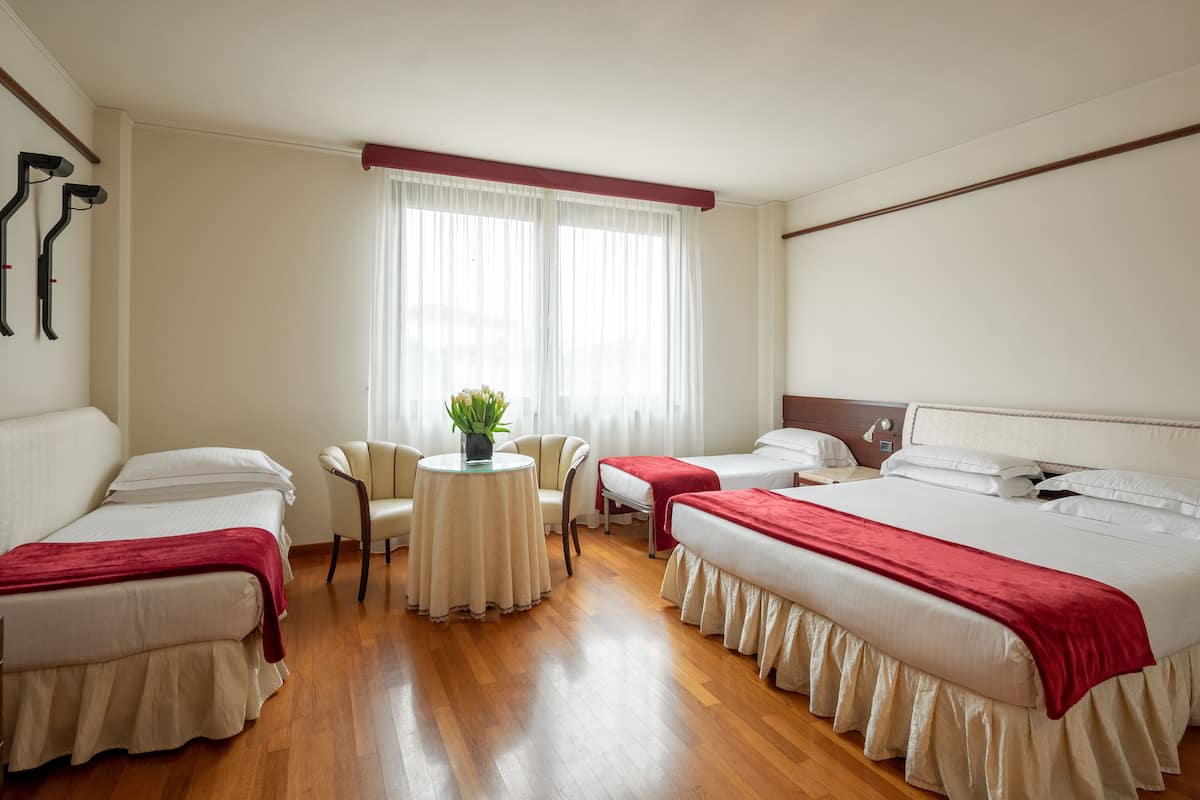 A hotel room with two beds, a round table with a plant, a chair, and a window with curtains.