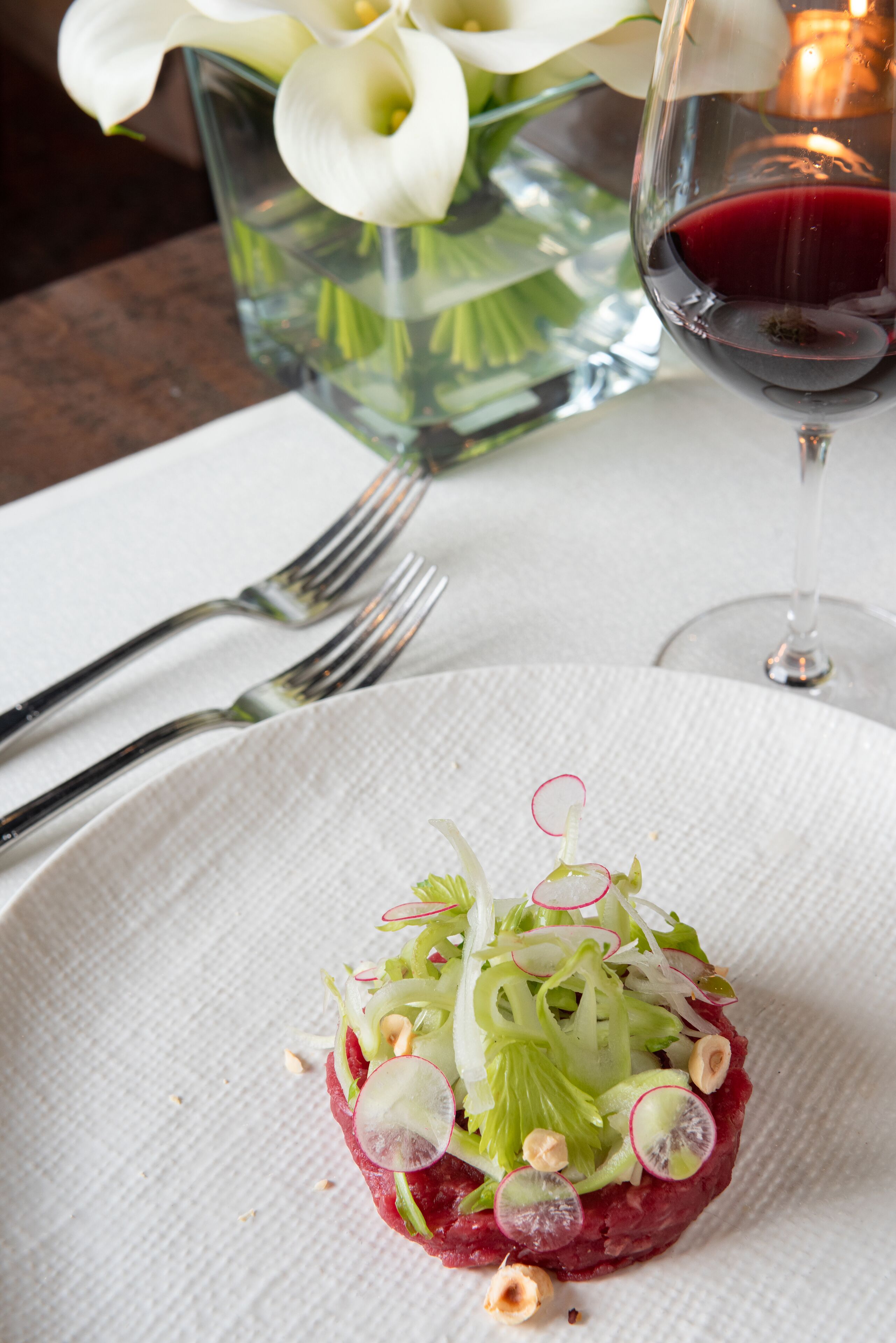 A plate of food with a glass of red wine and a vase of white flowers on the table.