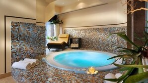 Ein moderner Spa-Bereich mit mosaikverkleideter Wand, einer runden Whirlwanne und einem Liegestuhl.